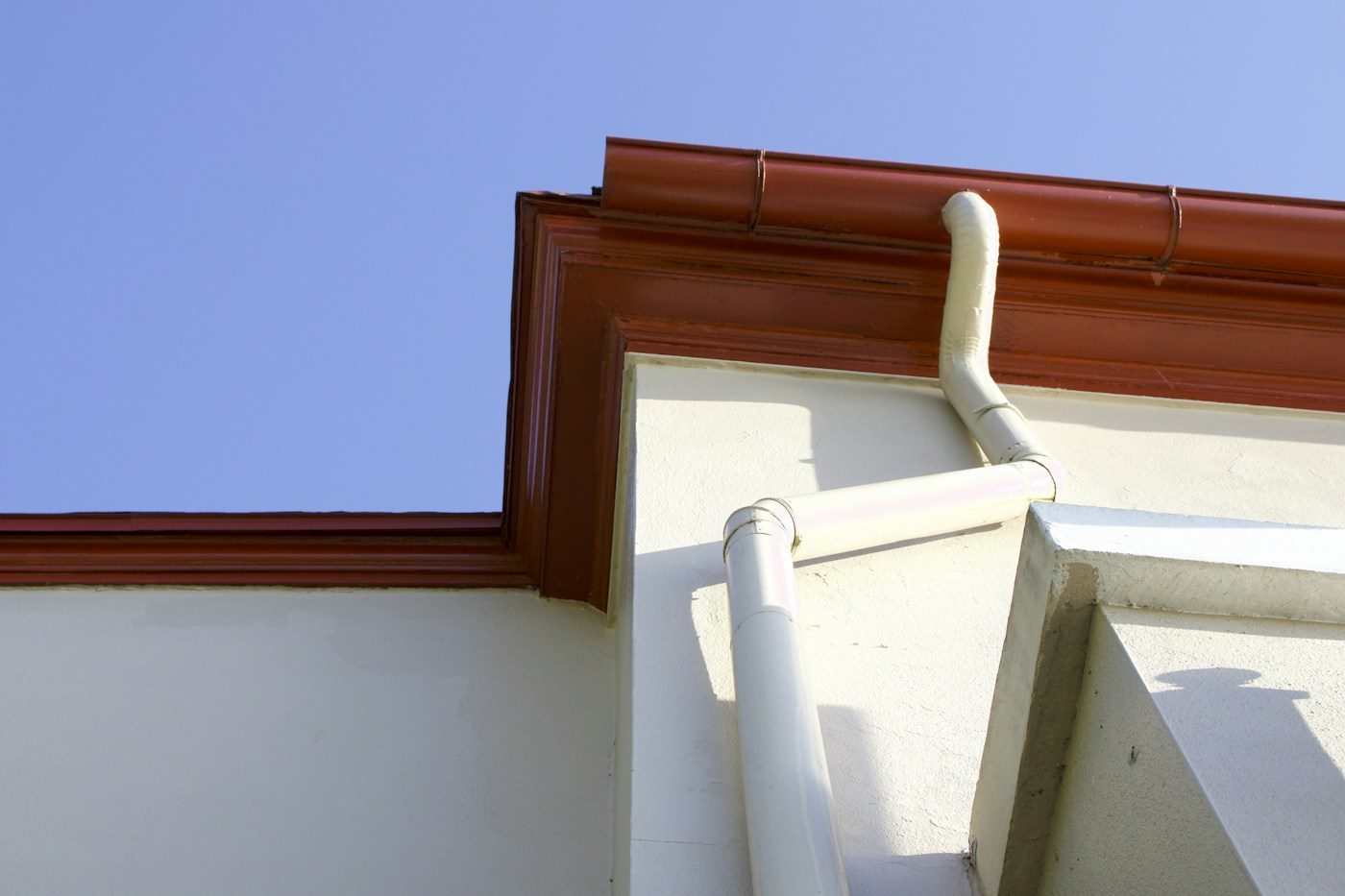 Clean gutter and downspout along a house roofline, ready for guard installation